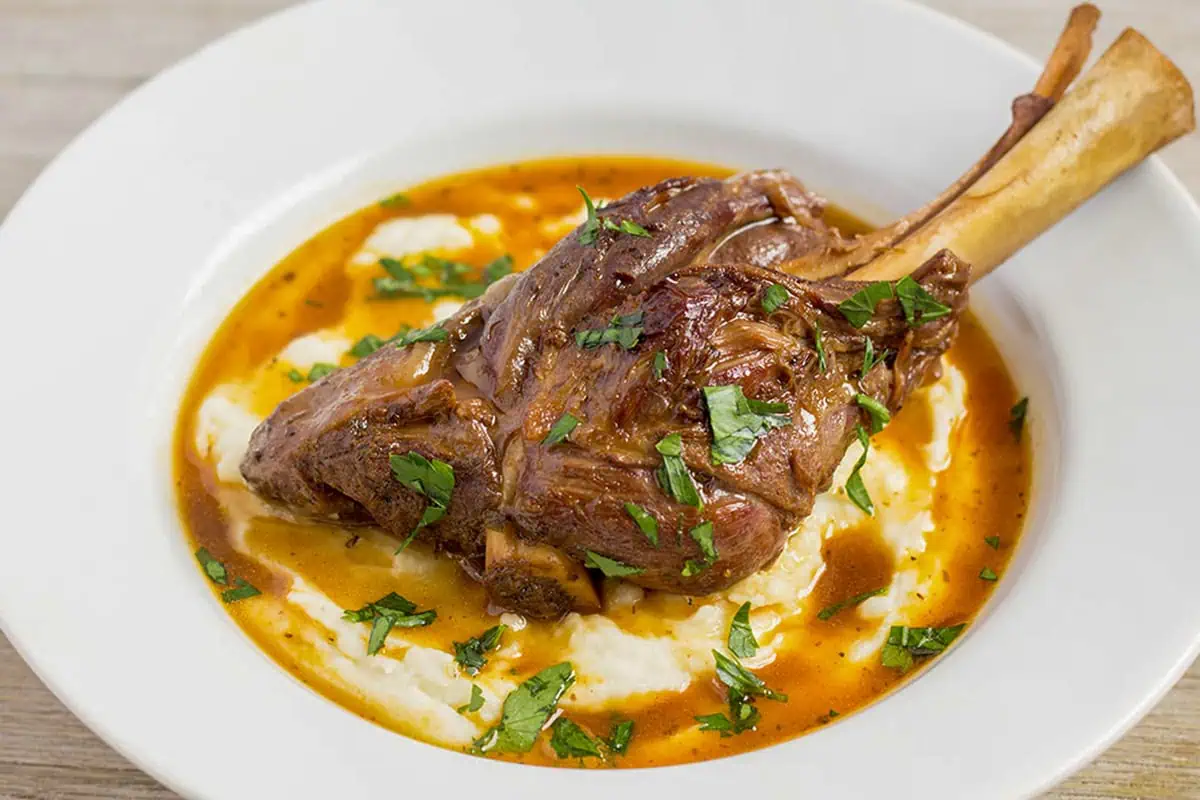 Pressure cooker lamb shank served over mashed potatoes with braising gravy and parsley in a white bowl.