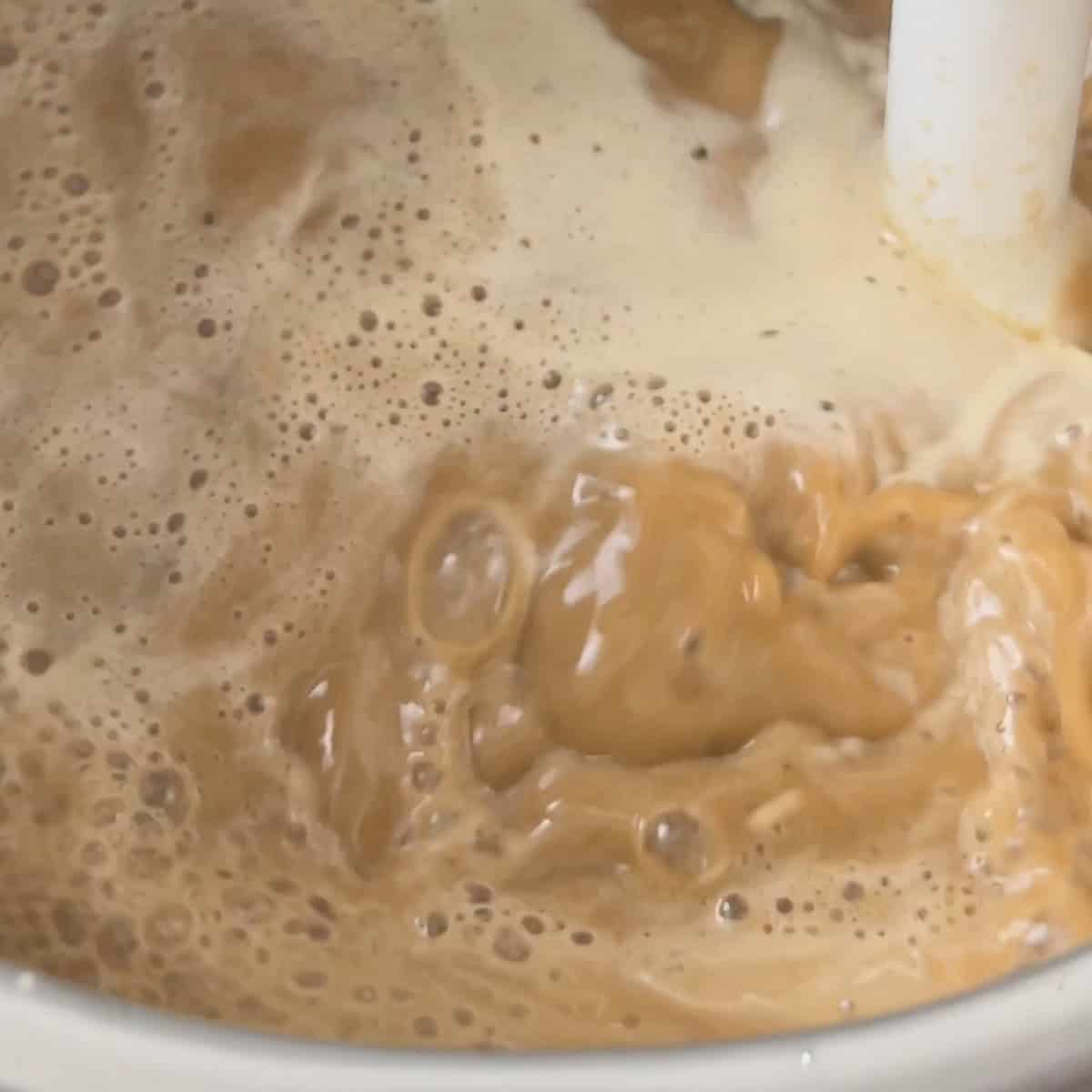 Lamb shank sauce being blended in the pot with an immersion blender until smooth and creamy.