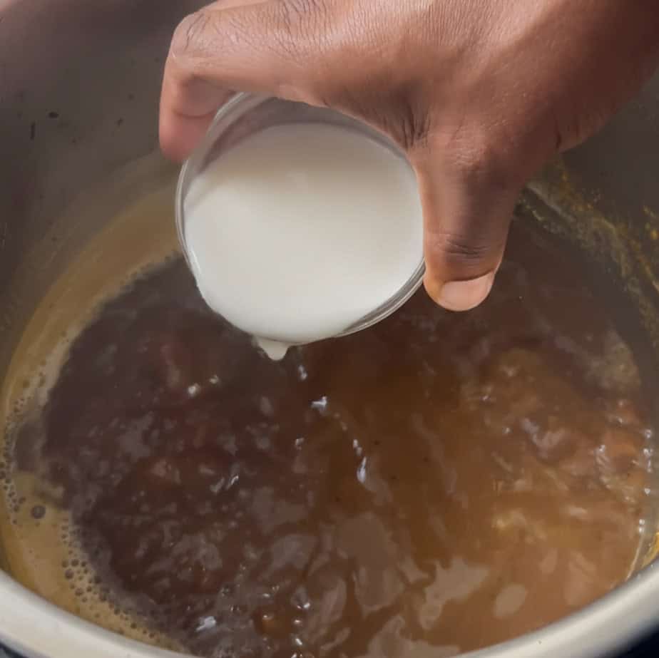 Hand pouring cornstarch slurry into simmering blended lamb shank sauce in the Instant Pot.