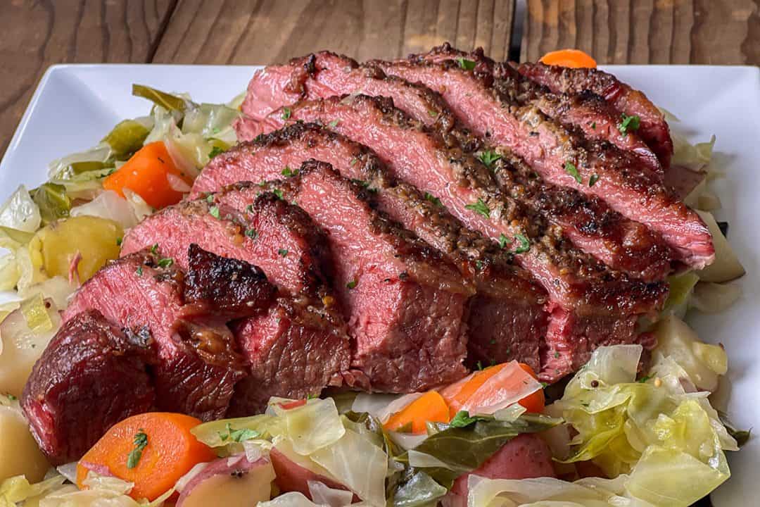 Sliced pressure cooker corned beef brisket served with cabbage, carrots, and potatoes on a white platter.