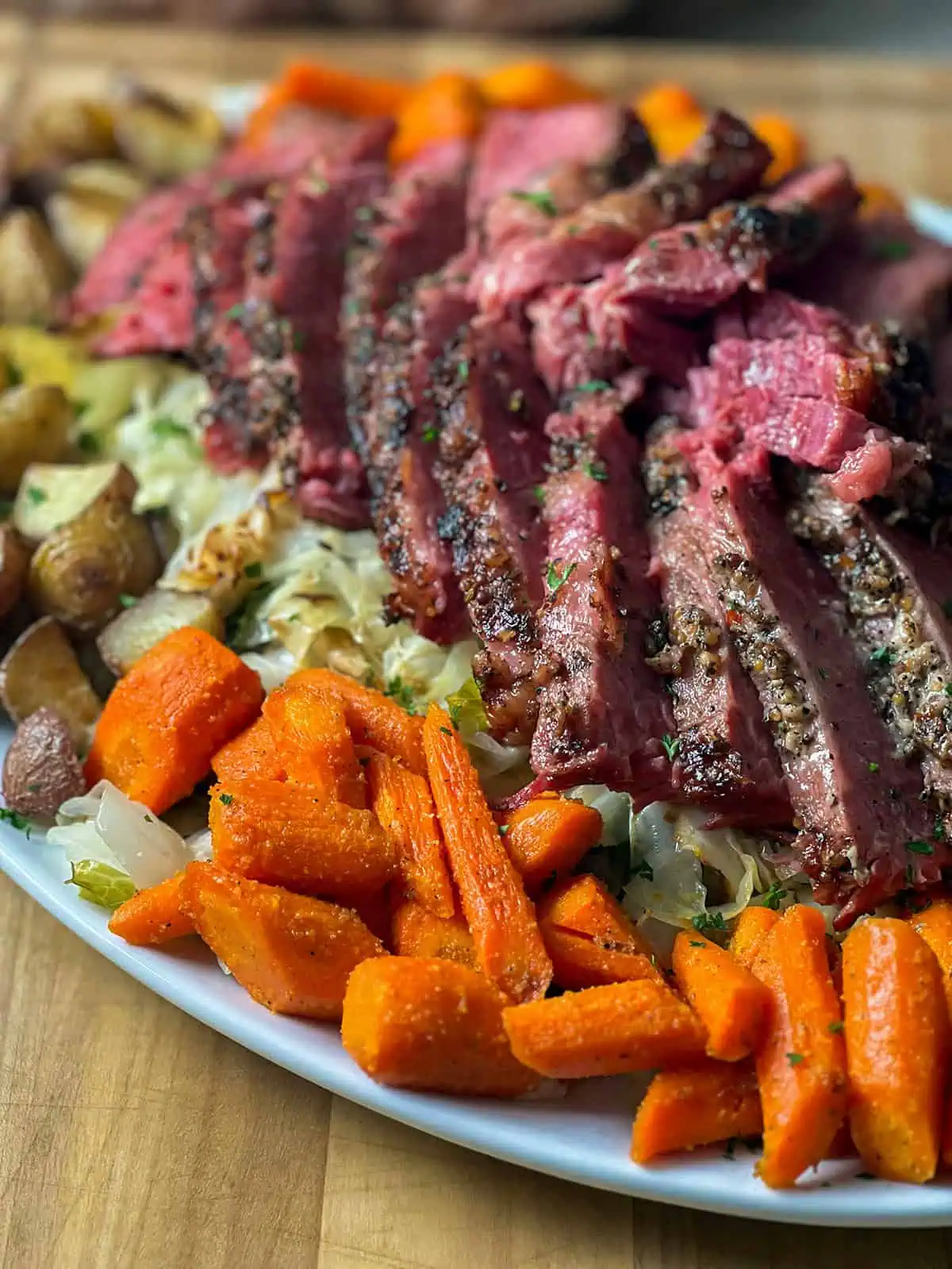 Sliced pressure cooker corned beef with crispy garlic top on a platter with cabbage, carrots, and potatoes.