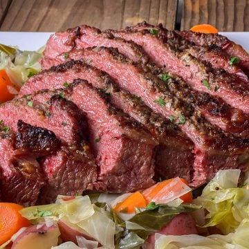 Sliced pressure cooker corned beef brisket served with cabbage, carrots, and potatoes on a white platter.