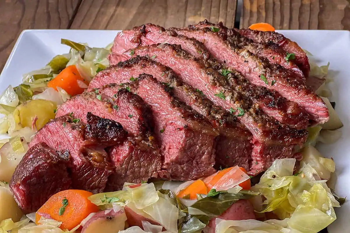 Sliced pressure cooker corned beef brisket served with cabbage, carrots, and potatoes on a white platter.