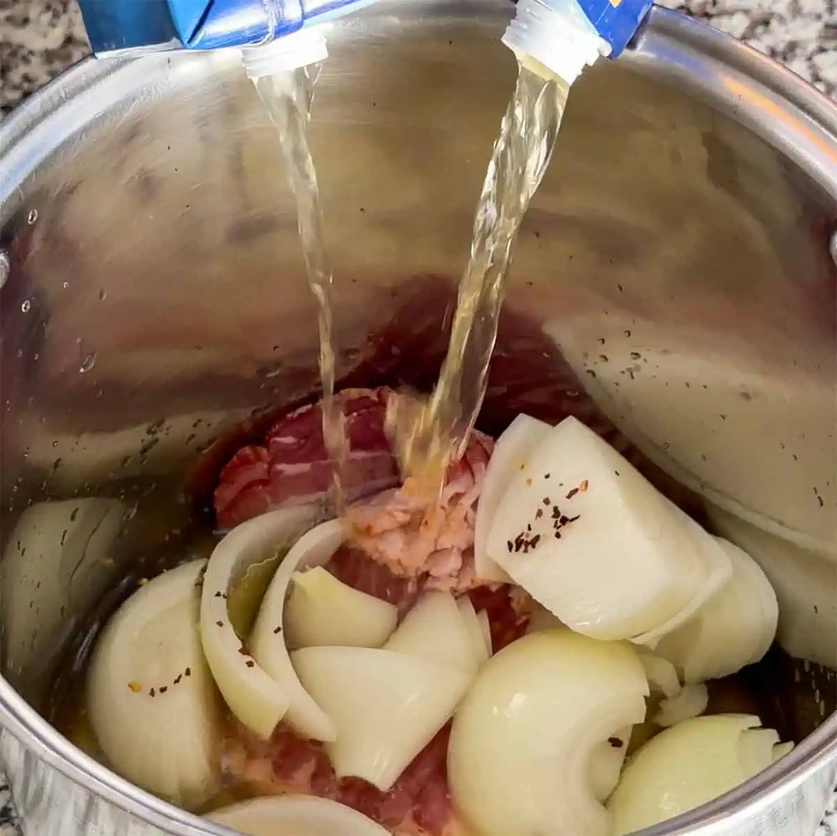 Chicken broth being poured into a stock pot with bacon and onions