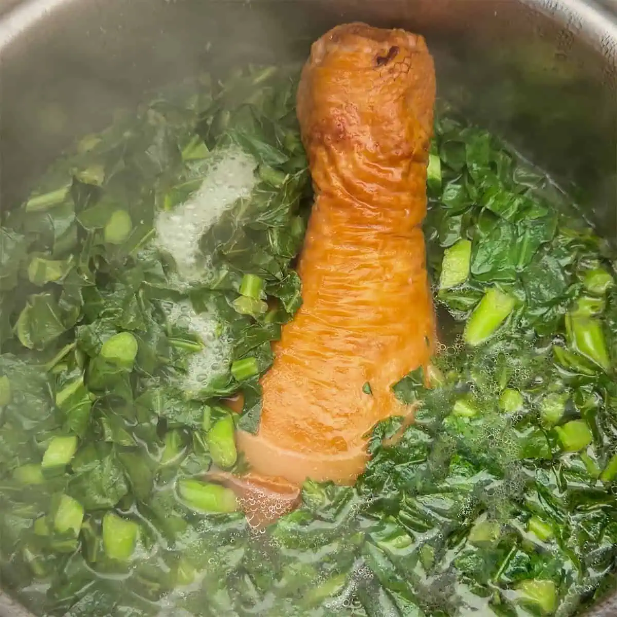 Collard greens and smoked turkey added to a pot of strained broth