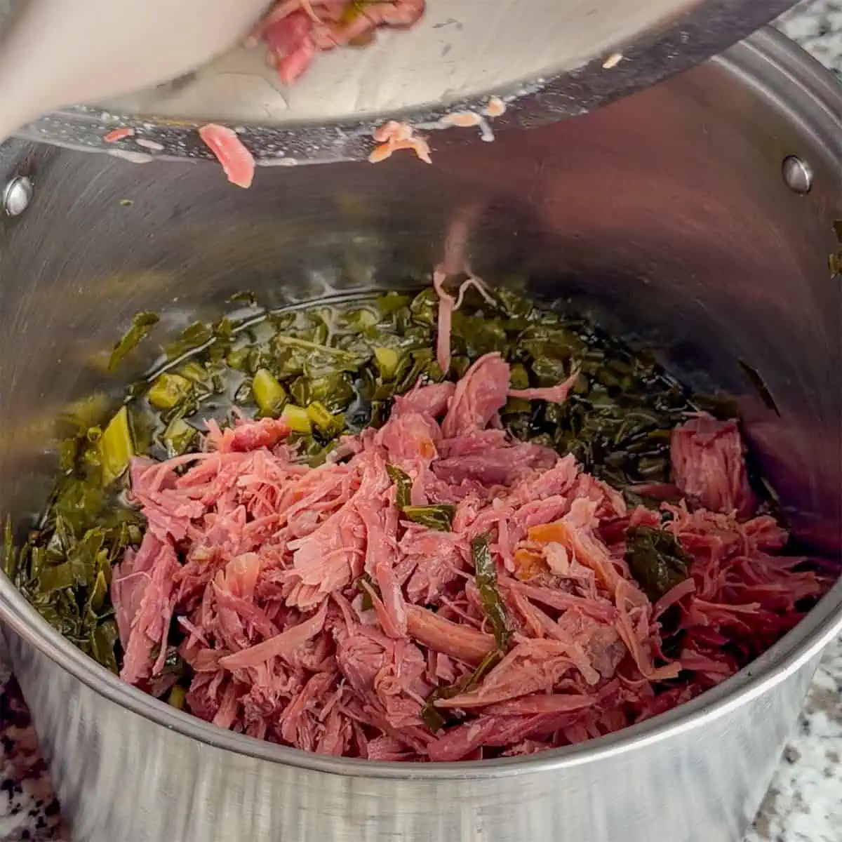 Shredded smoked turkey being added back to a pot of collard greens