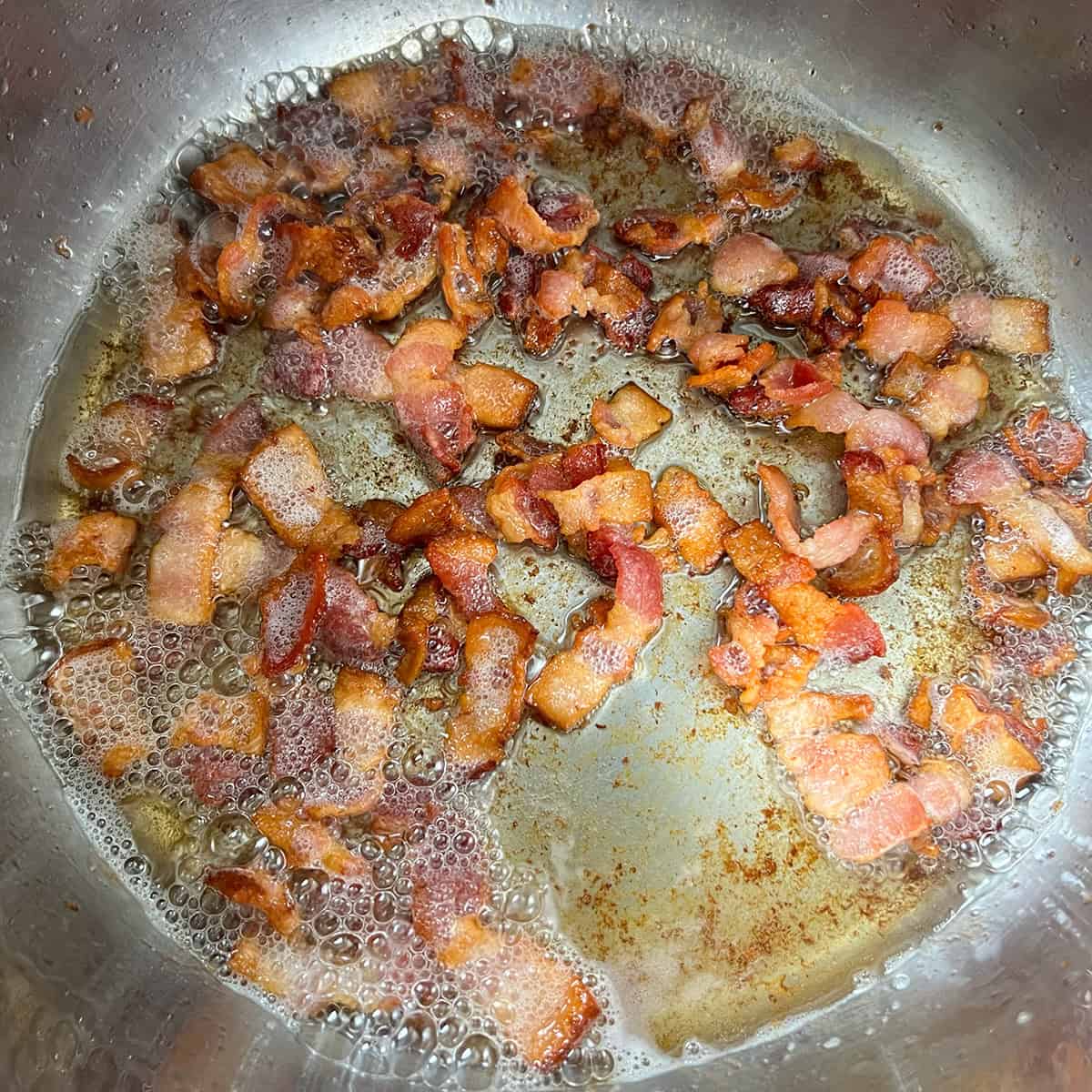 Bacon cooking in a pot until browned and rendered.