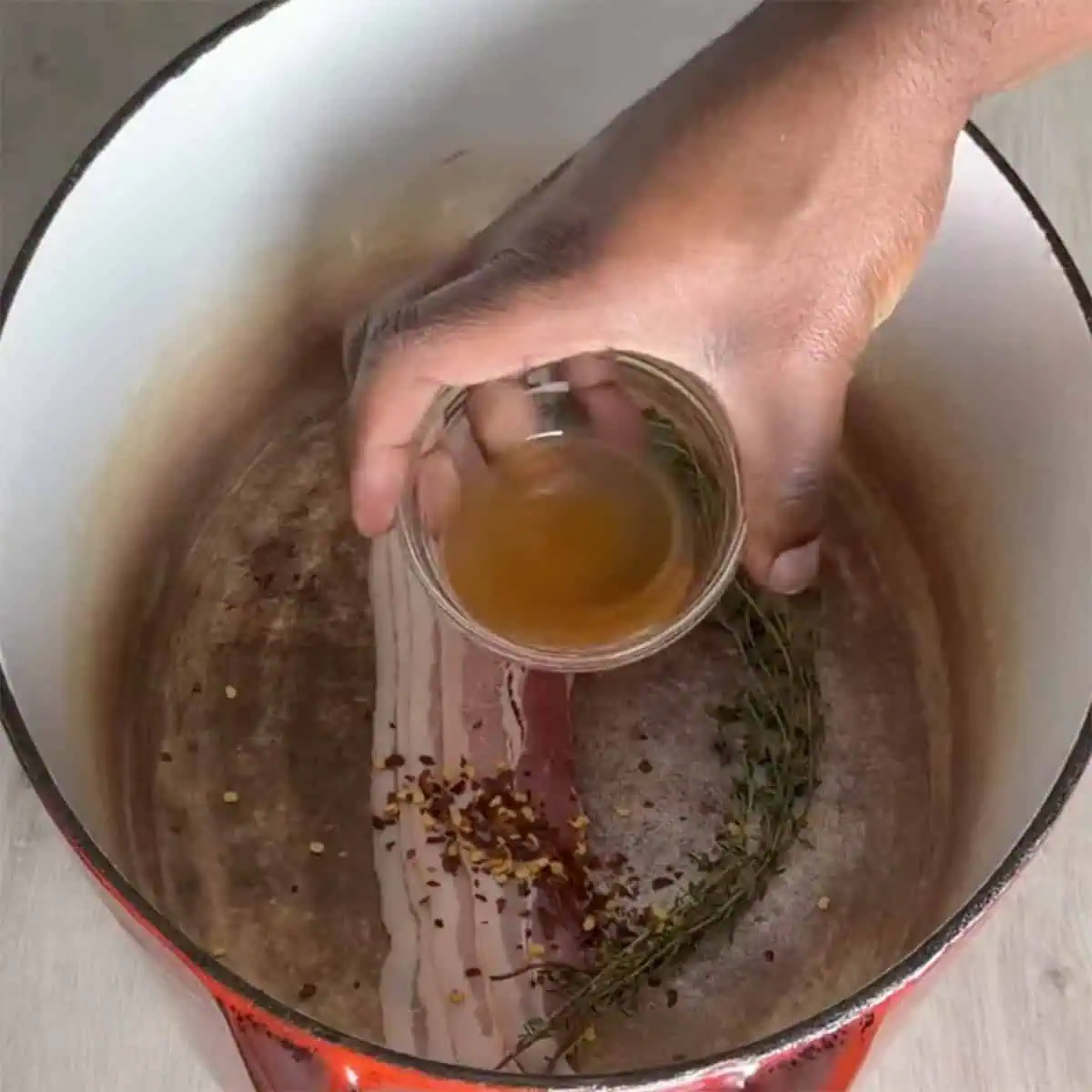 Adding vinegar to the pot with bacon and seasonings for collard greens.