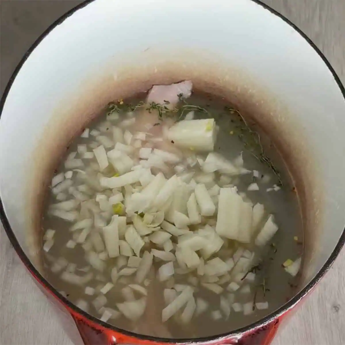 Chopped onions in broth with herbs in a Dutch oven.