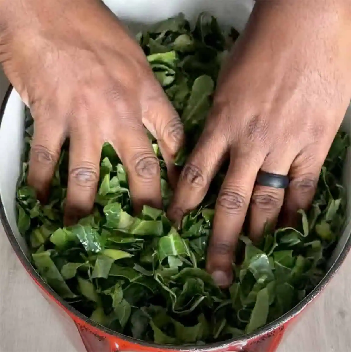 Hands pressing fresh chopped collards down into a Dutch oven.
