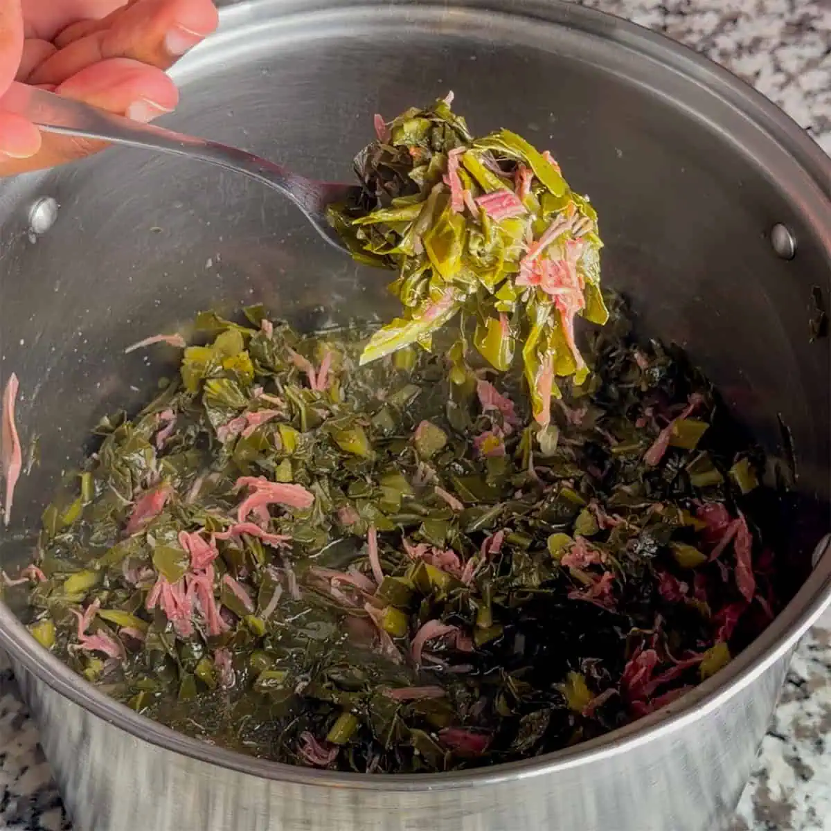 Fork lifting collard greens with shredded smoked turkey from a pot