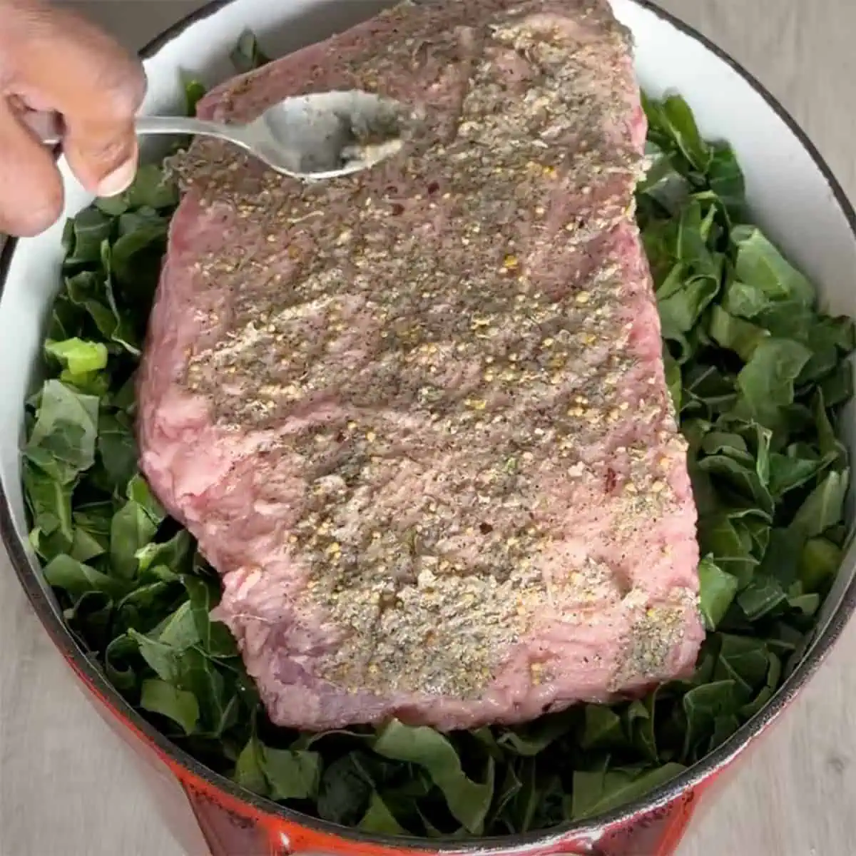 Spreading seasoning on corned beef laid over collards in a Dutch oven.