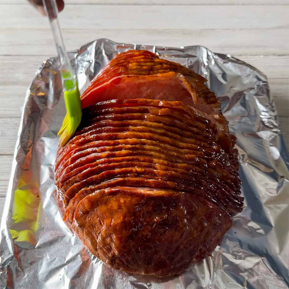 Brushing glaze over a spiral-cut ham before adding the brown sugar crust.