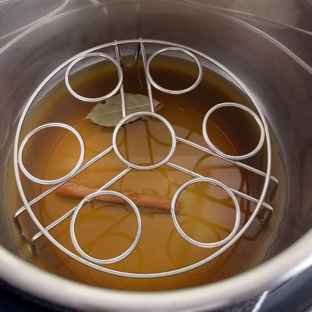 Instant Pot with apple cider, cinnamon stick, bay leaf, and trivet set up for warming ham.