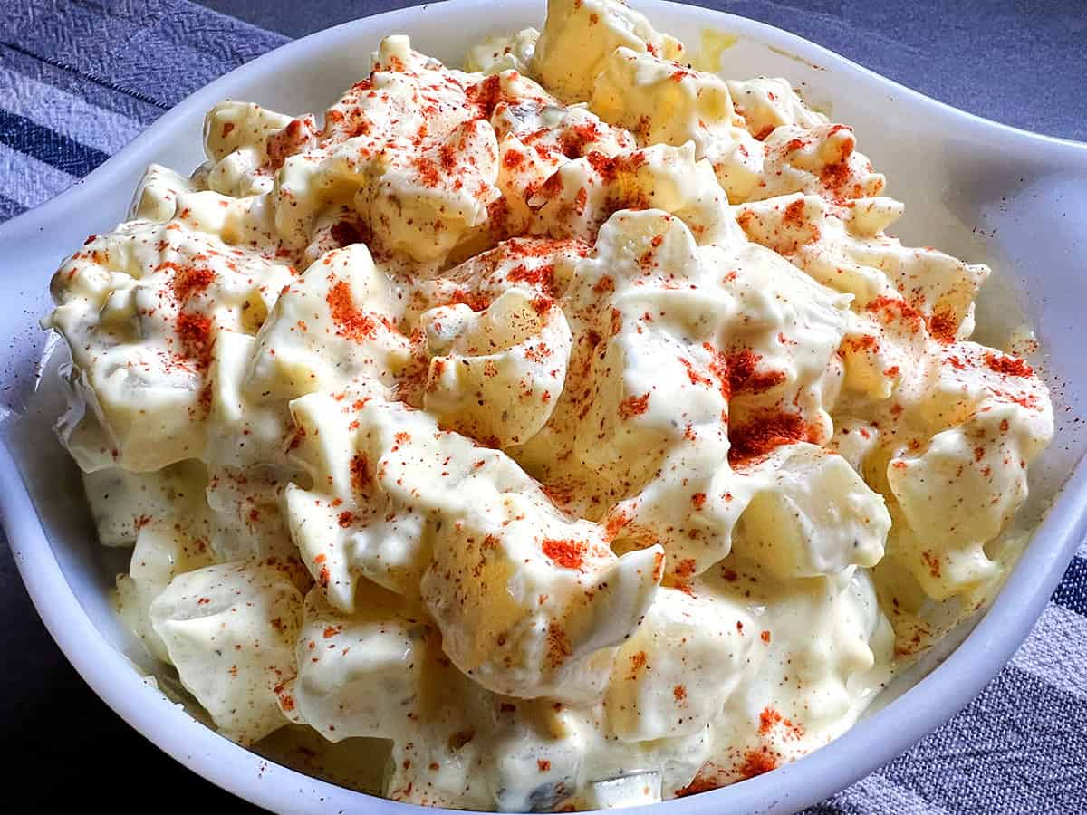 Angled close view of deviled egg-style potato salad in a white serving dish with paprika on top.