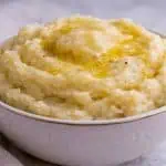 A white bowl filled with creamy mashed potatoes topped with melted butter and cracked black pepper.