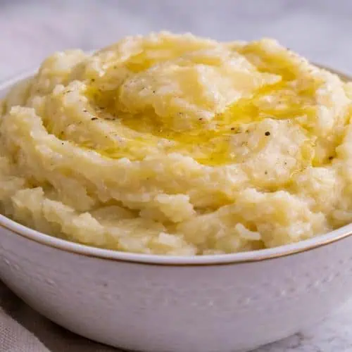 Bowl of creamy mashed potatoes made with evaporated milk, topped with melted butter and black pepper.
