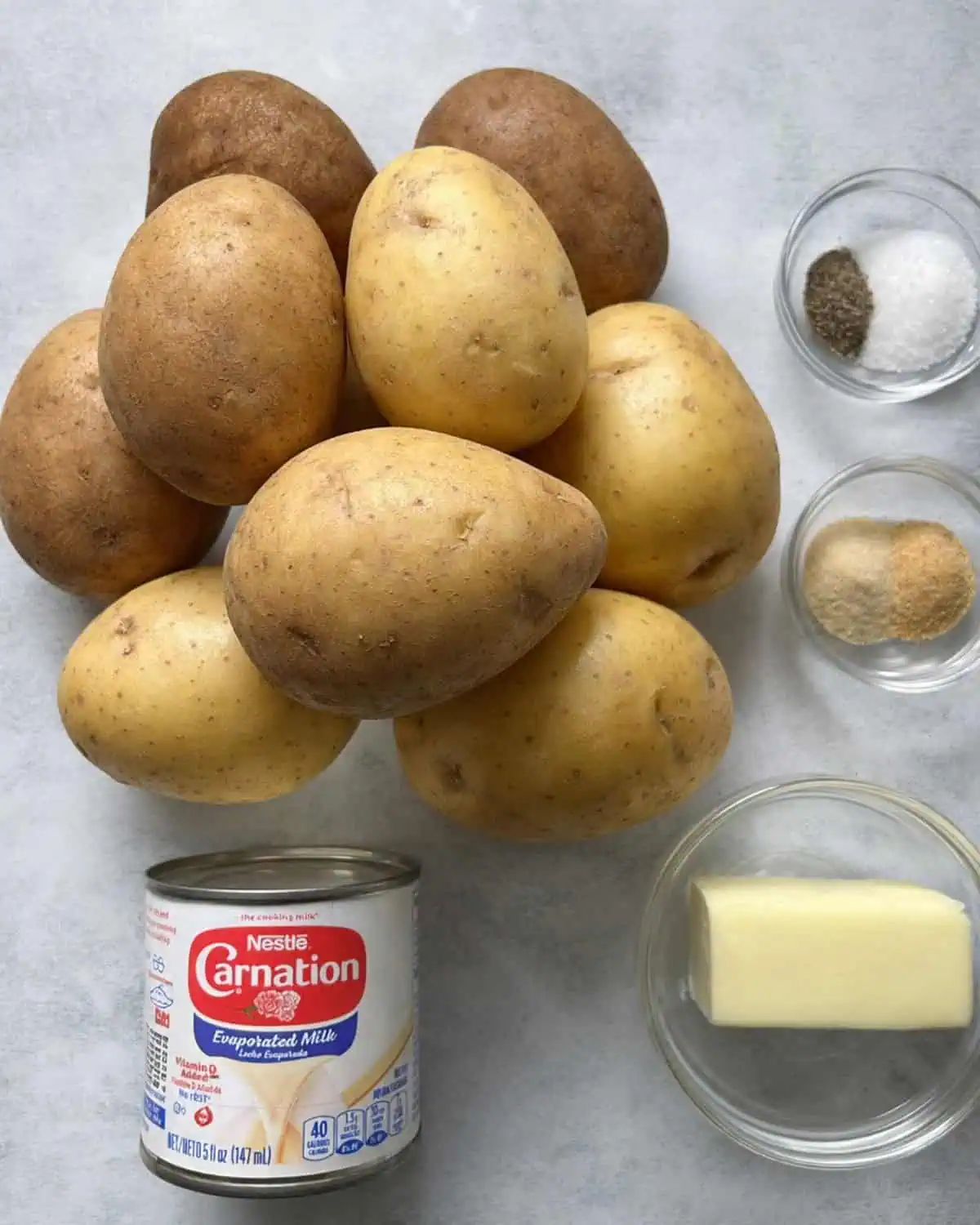 Ingredients for mashed potatoes with evaporated milk, including Yukon Gold potatoes, russet potatoes, butter, seasonings, and evaporated milk