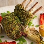 Mint-crusted rack of lamb on a plate with roasted fennel, red bell pepper, and grilled lemon