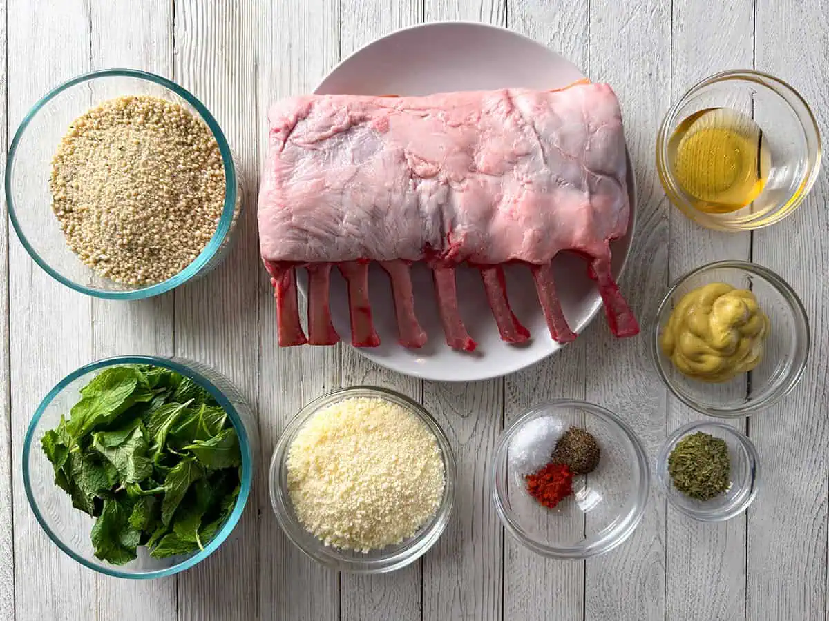 Ingredients for mint-crusted rack of lamb including frenched lamb rack, breadcrumbs, fresh mint, Parmesan, olive oil, Dijon mustard, and seasonings