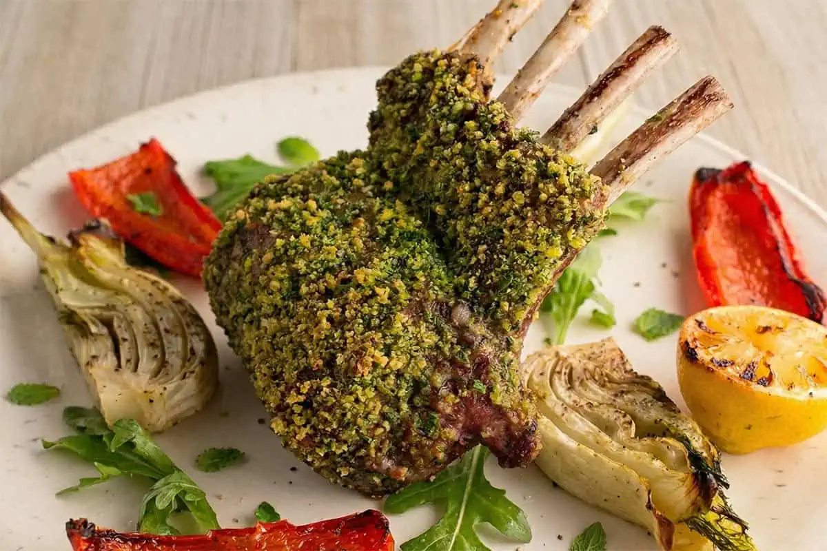 Plated mint-crusted rack of lamb with roasted fennel, red bell pepper, arugula, and grilled lemon