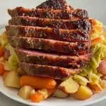 Close view of sliced oven corned beef with a crispy top served over cabbage, carrots, and potatoes