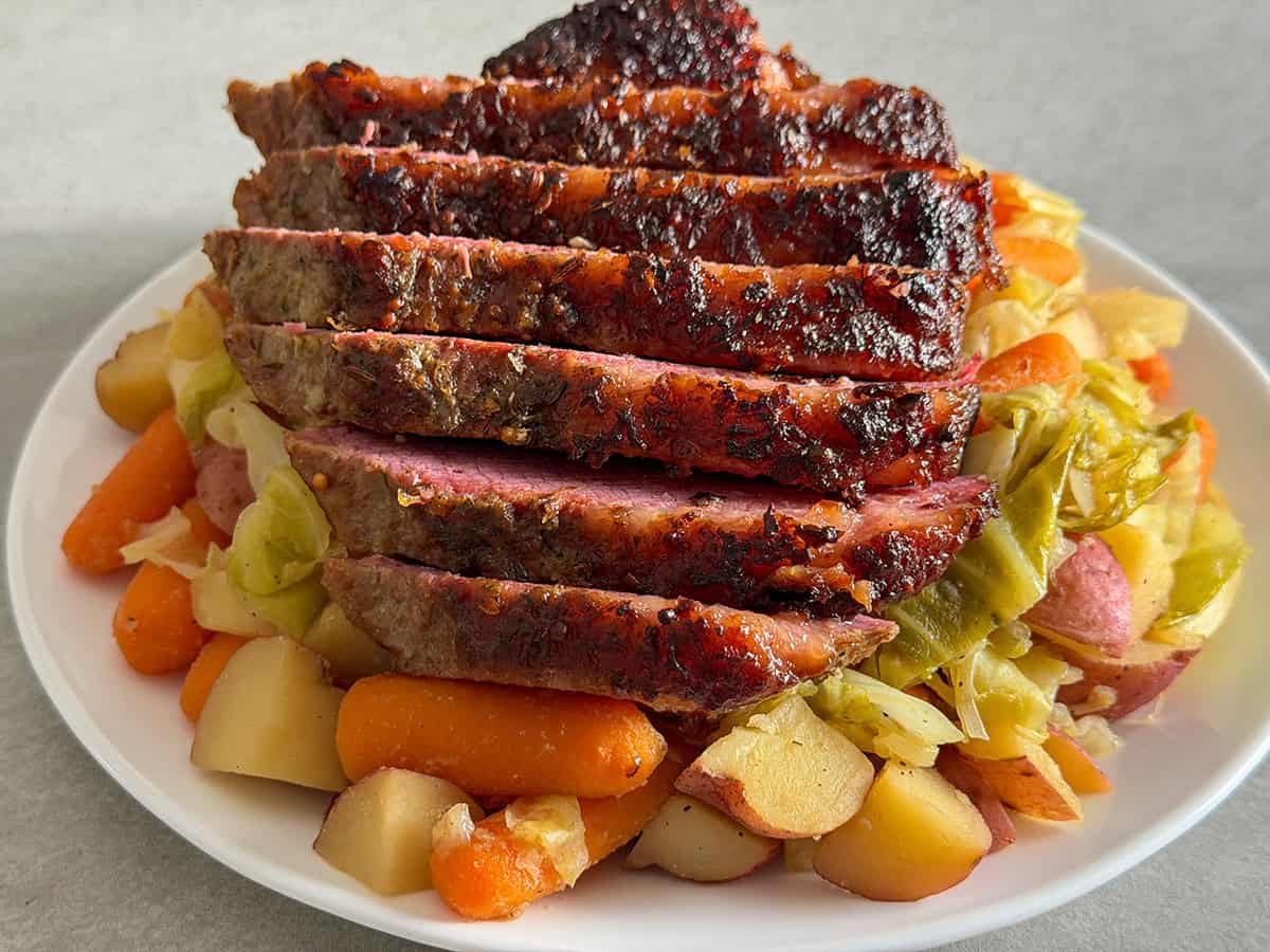 Close view of sliced oven corned beef with a crispy top served over cabbage, carrots, and potatoes