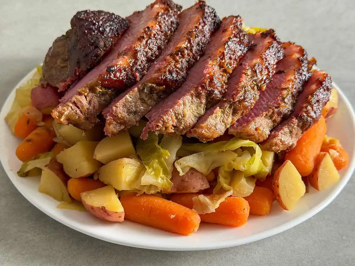 Oven baked corned beef sliced and served over cabbage, carrots, and red potatoes on a white plate