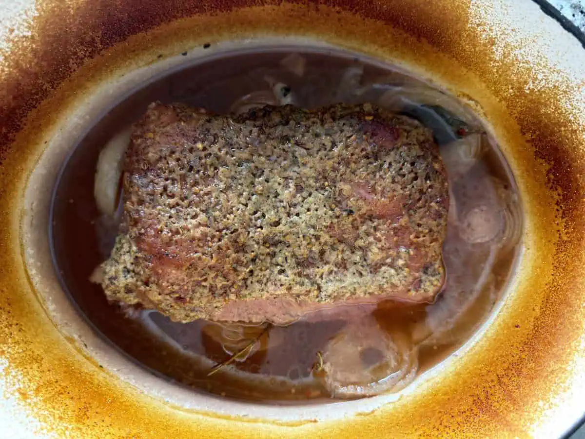 Oven corned beef braising in a Dutch oven with onions and broth