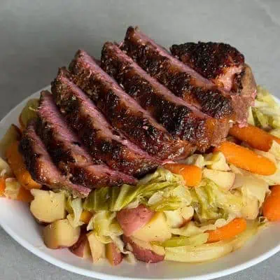 Close-up of sliced oven corned beef showing the crispy seasoned crust over cabbage, carrots, and potatoes