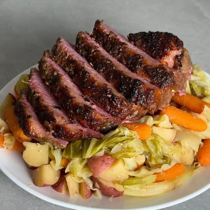 Close-up of sliced oven corned beef showing the crispy seasoned crust over cabbage, carrots, and potatoes