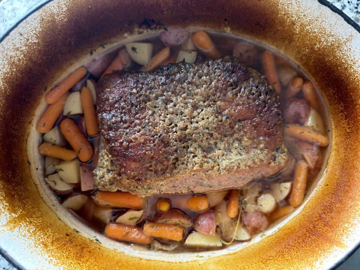 Oven corned beef returned to the Dutch oven on top of carrots and potatoes