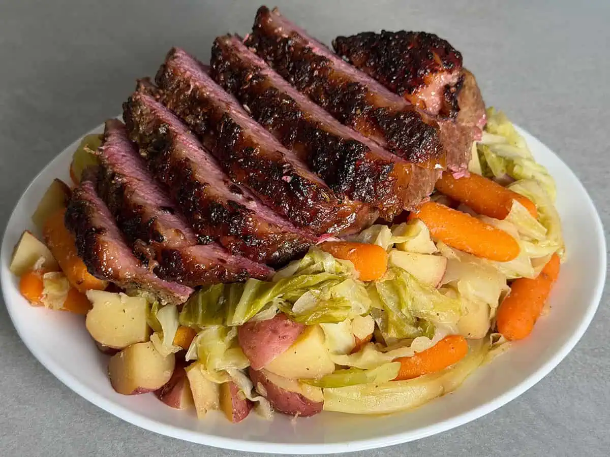 Close-up of sliced oven corned beef with browned crust and pink center over cooked vegetables