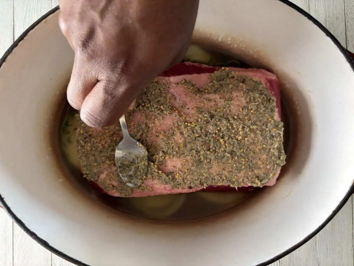 Garlic and spice paste being spread over the fat cap of corned beef in a Dutch oven.
