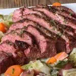 Sliced pressure cooker corned beef served with cabbage, carrots, and red potatoes on a white platter