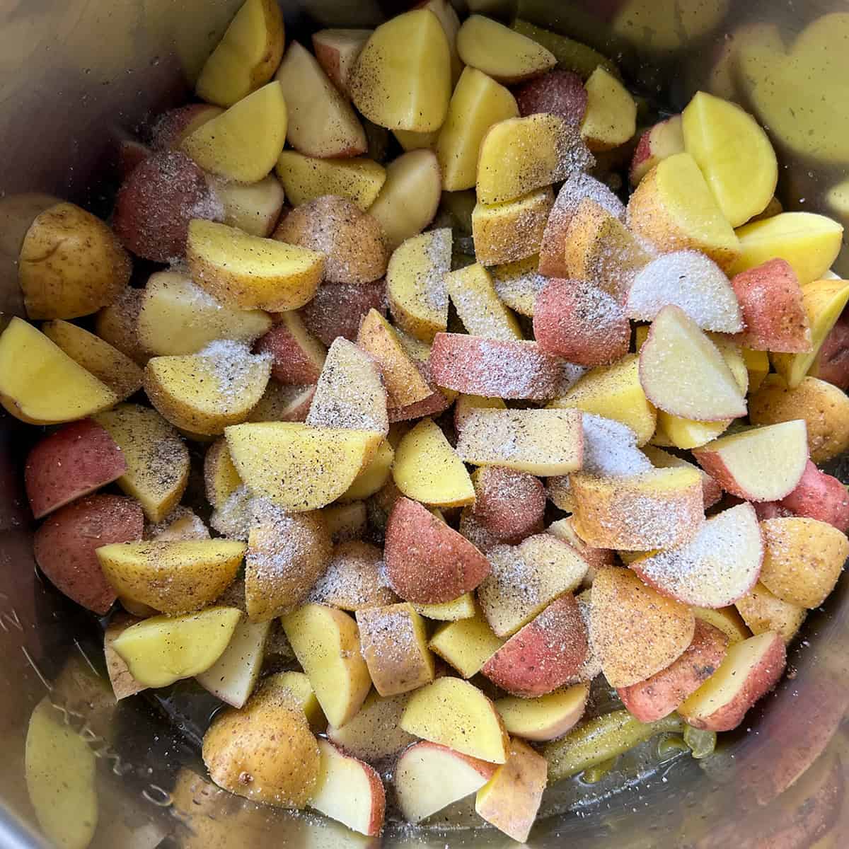 Chopped red and gold potatoes seasoned with salt and pepper over green beans in the pot.