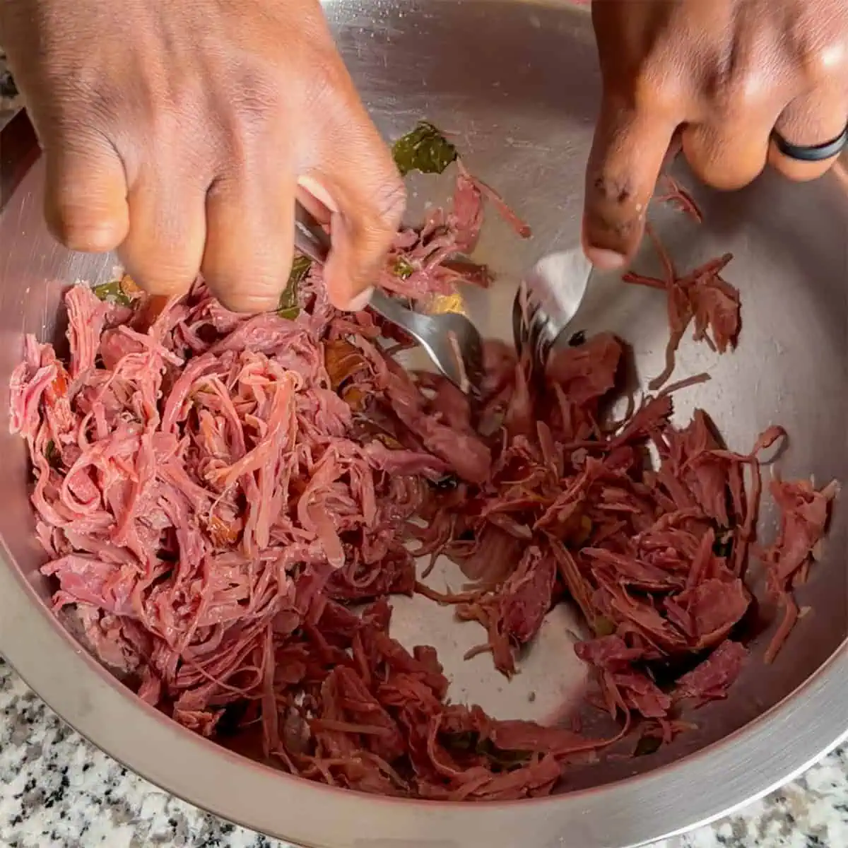Smoked turkey being shredded with forks in a metal bowl