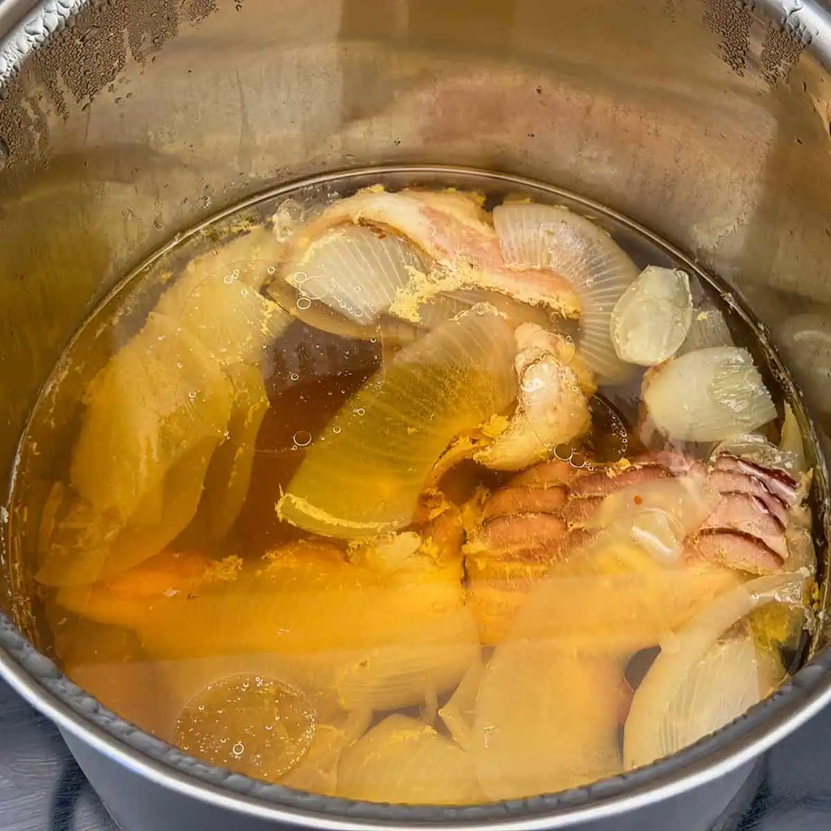 Bacon and onions simmering in broth in a large stock pot