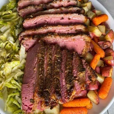 Overhead view of sliced slow cooker corned beef with crispy garlic top served with cabbage, carrots, and red potatoes.