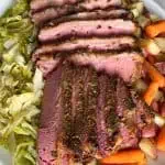 Overhead view of sliced slow cooker corned beef with crispy garlic top served with cabbage, carrots, and red potatoes.