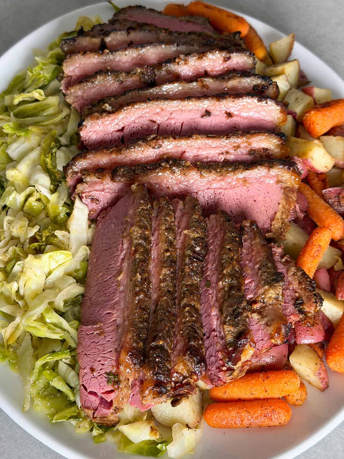 Overhead view of sliced slow cooker corned beef with crispy garlic top served with cabbage, carrots, and red potatoes.