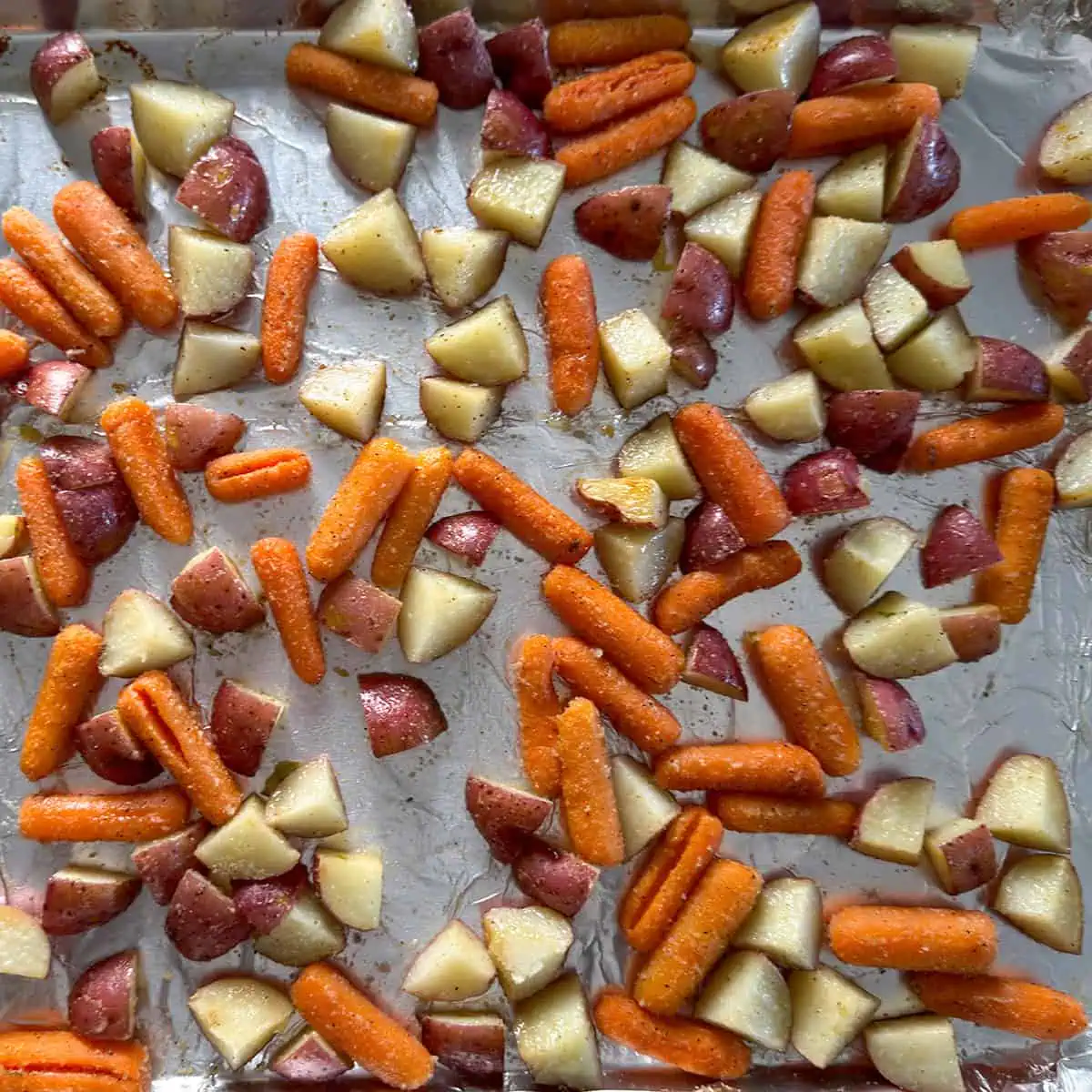 Roasted red potatoes and carrots finishing on a sheet pan after the cabbage has been removed.