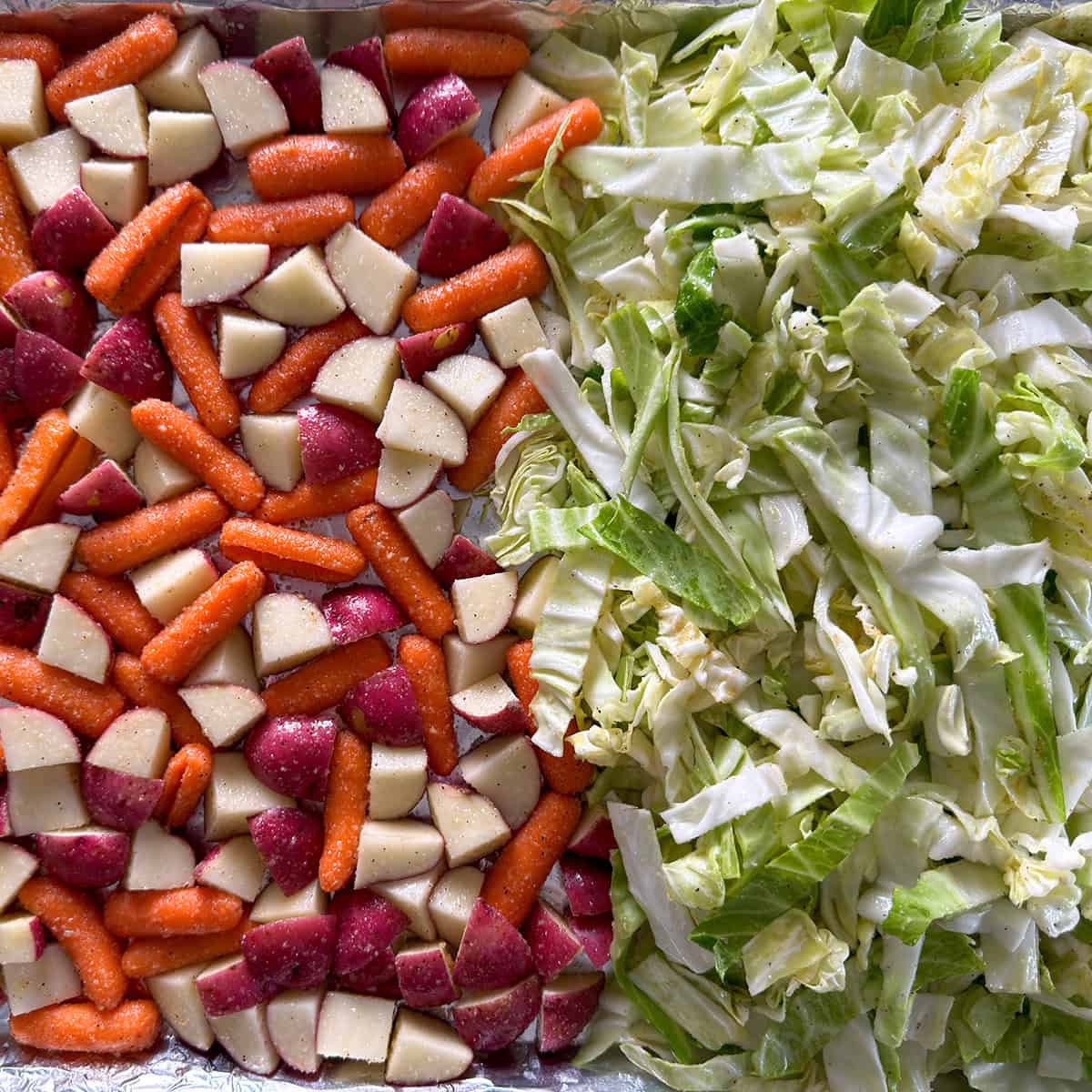 Close-up of seasoned cabbage, carrots, and red potatoes on a sheet pan before roasting.