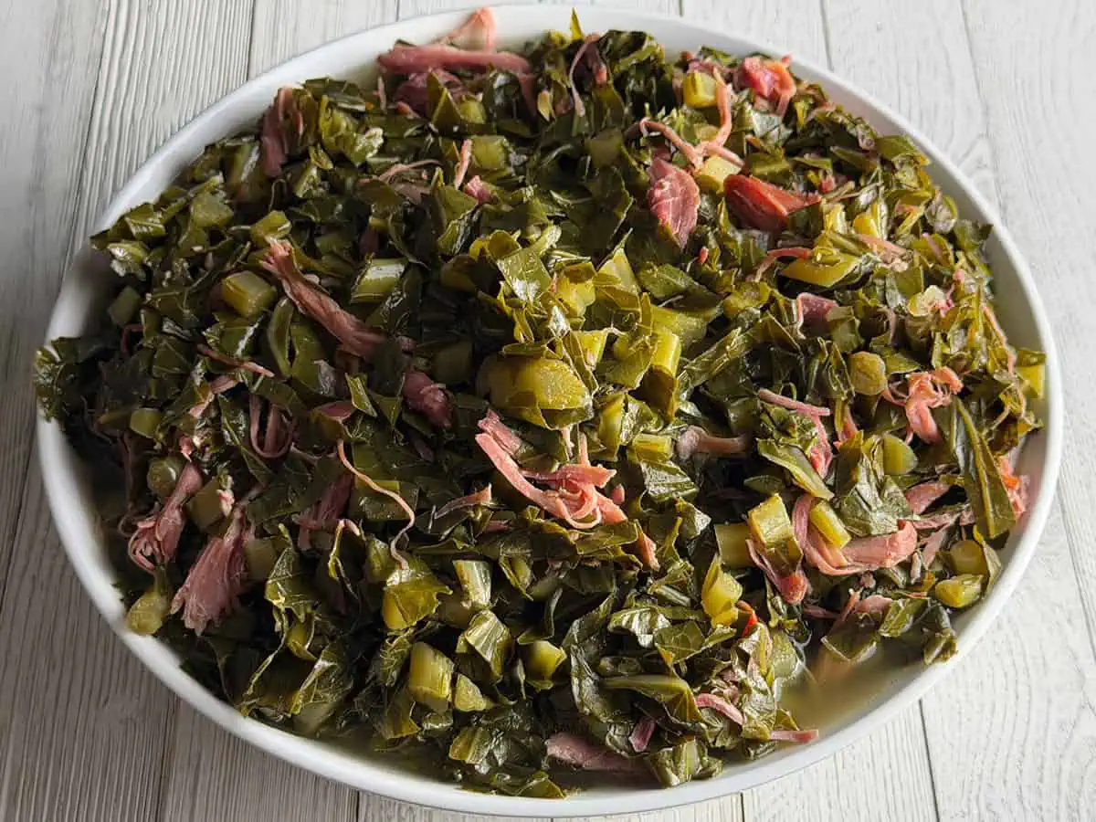 Serving bowl filled with tender collard greens and pieces of smoked turkey