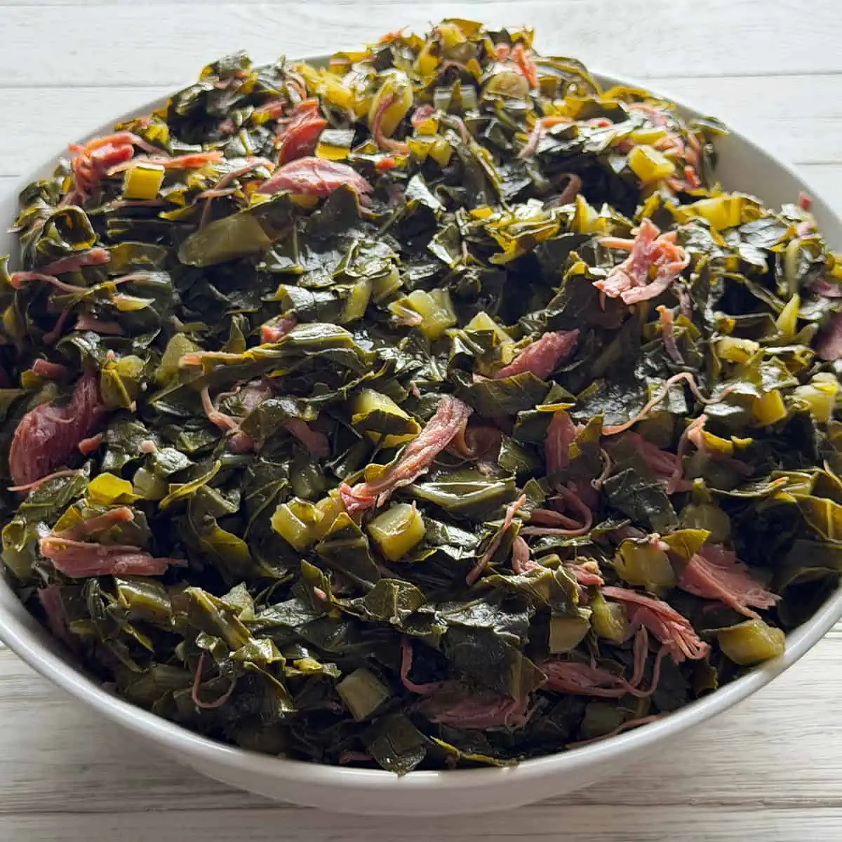 Bowl of southern collard greens cooked with smoked turkey, chopped onions, and pot liquor