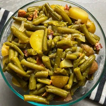 Overhead view of southern green beans with potatoes, bacon, and onions in a glass bowl.