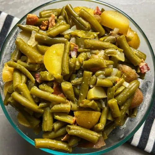 Overhead view of southern green beans with potatoes, bacon, and onions in a glass bowl.