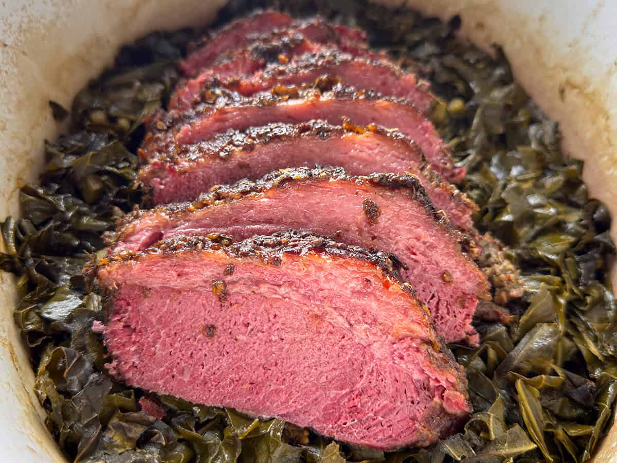 Sliced southern style corned beef over braised collard greens in a Dutch oven