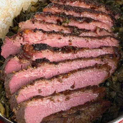 Sliced corned beef with a dark crust served over greens in a Dutch oven.