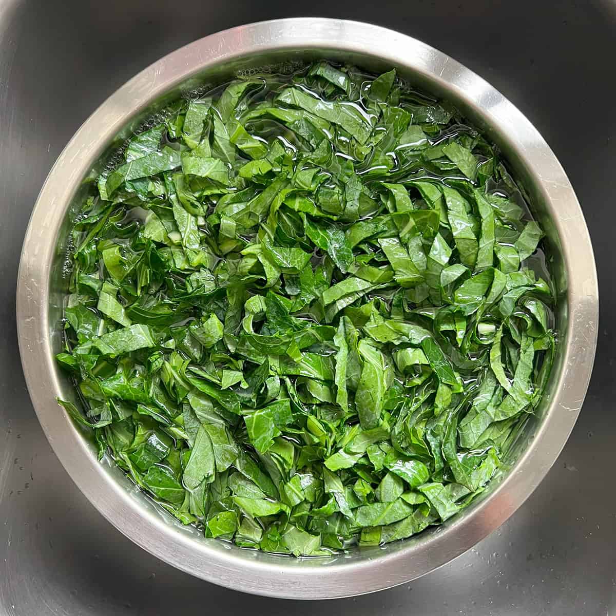 Shredded collard greens soaking in water in a metal bowl